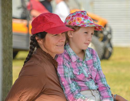 A woman sits with a girl on her lap as they both watch something. 